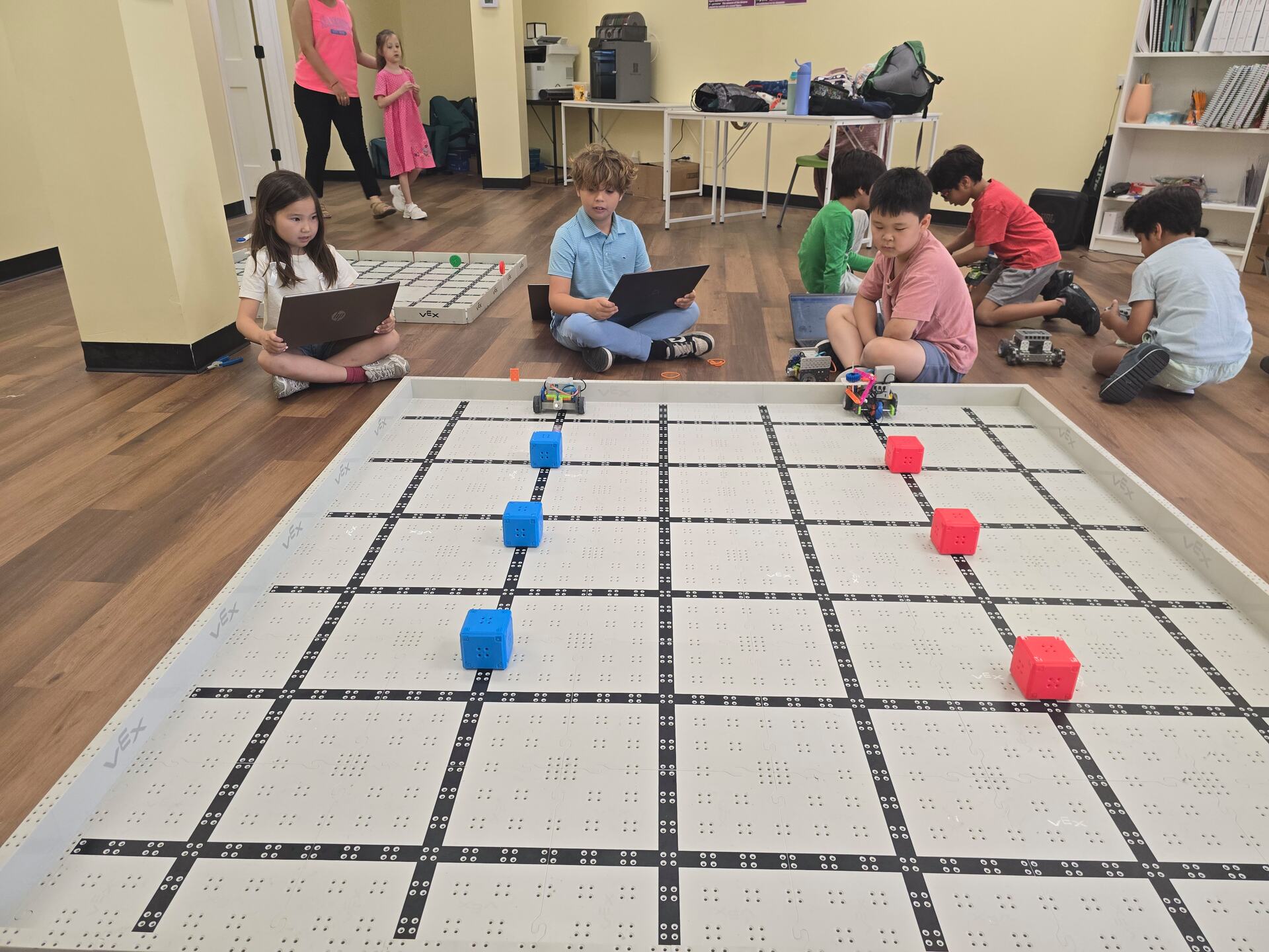 Campers programming robots on laptops beside a robotics field