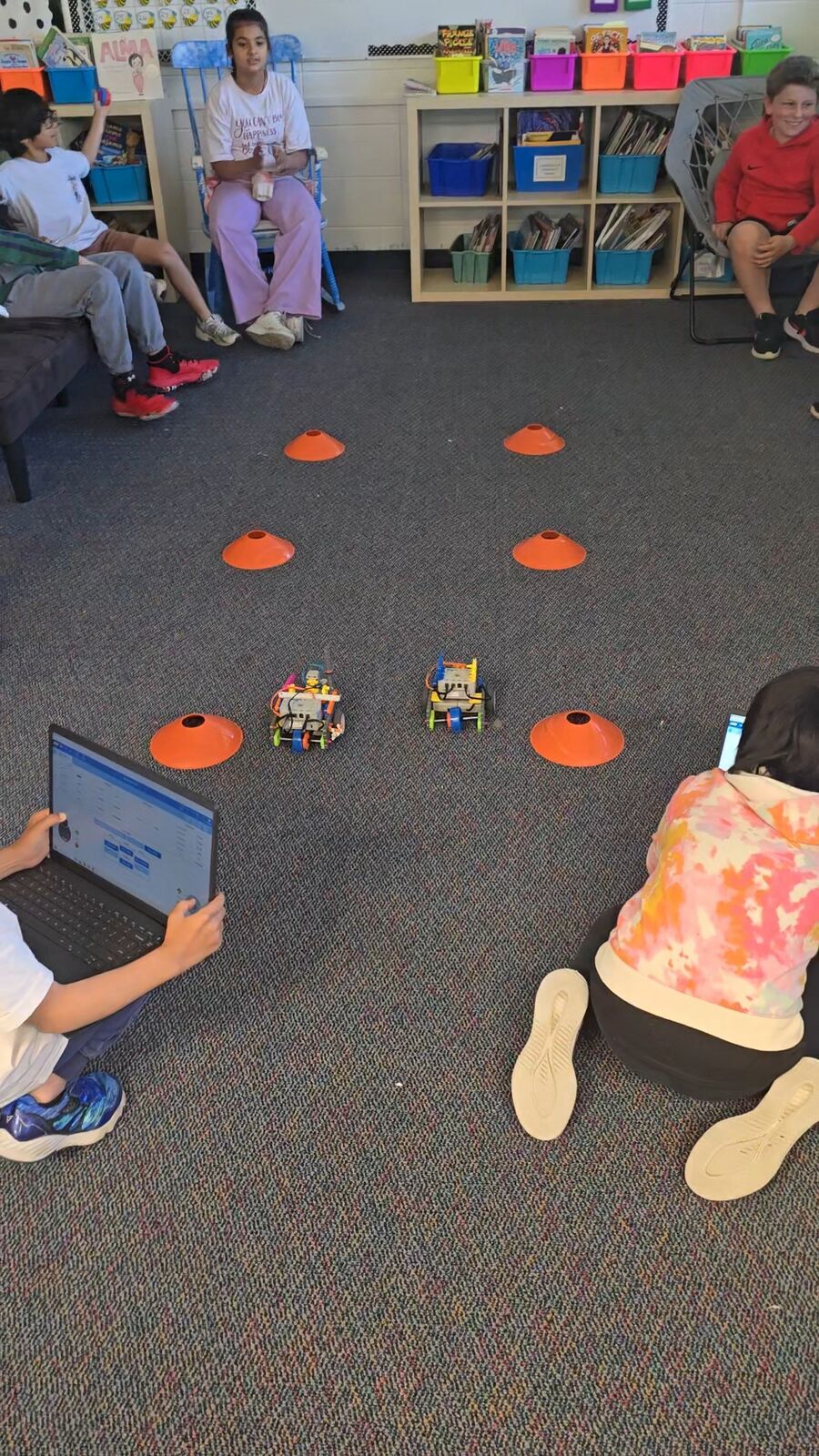Student-built robots running a cone course while classmates watch